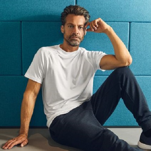 man in white t shirt, jeans, posing against blue brick wall