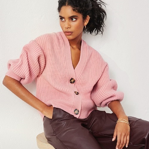 woman in pink sweater brown pants, posing on stool